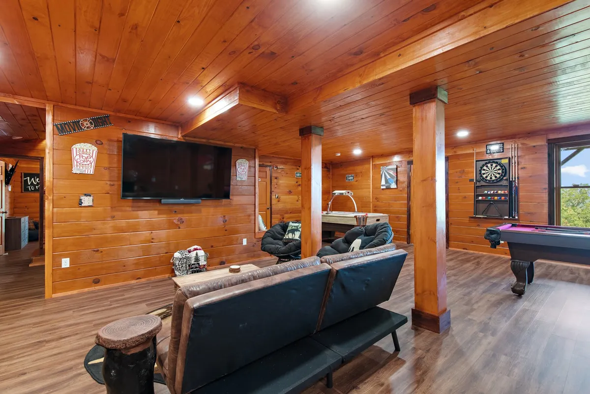A comfortable, entertainment-focused room with a pool table, dart board, flat-screen television, and a seating area for socializing. The setup invites both active play and relaxed spectating, supporting group entertainment and downtime between games.