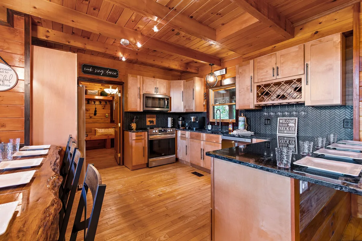 This image offers a view of the kitchen area, showcasing the kitchen island, stainless steel appliances, a wooden dining table, and cabinets with glass doors. The scene exudes a cozy, inviting mood, ideal for preparing group meals and casual countertop dining.