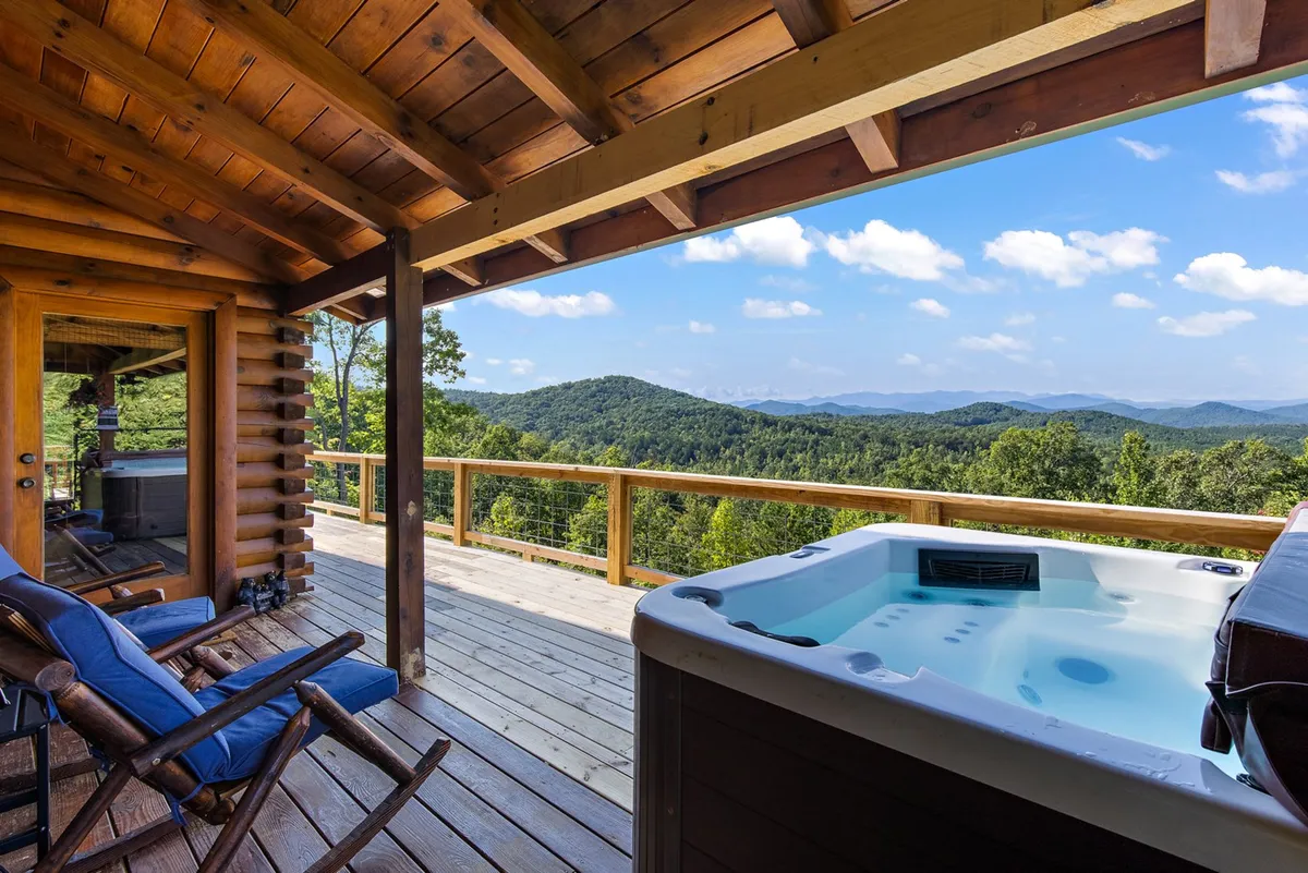 This image captures a stunning outdoor deck featuring a hot tub with a panoramic view of the Blue Ridge Mountains. Wooden beams frame the space, and the tranquil setting invites relaxation and socializing as the sun sets or stars appear overhead.