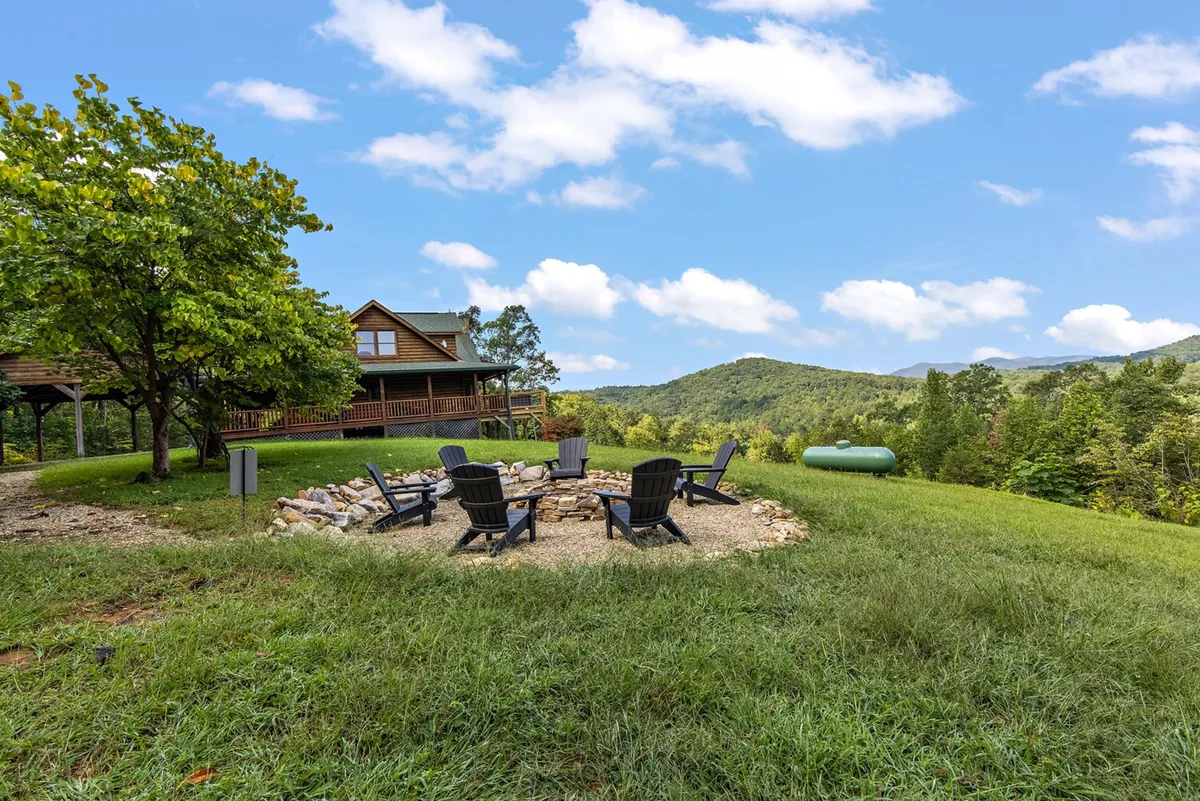This exterior image features a welcoming fire pit surrounded by Adirondack chairs with a mountain view, the house, and a nearby tree. The setting is cozy and inviting, perfect for gathering, sharing stories, and enjoying sunsets or stargazing, which aligns with the fire pit and Adirondack chairs highlighted in the section.