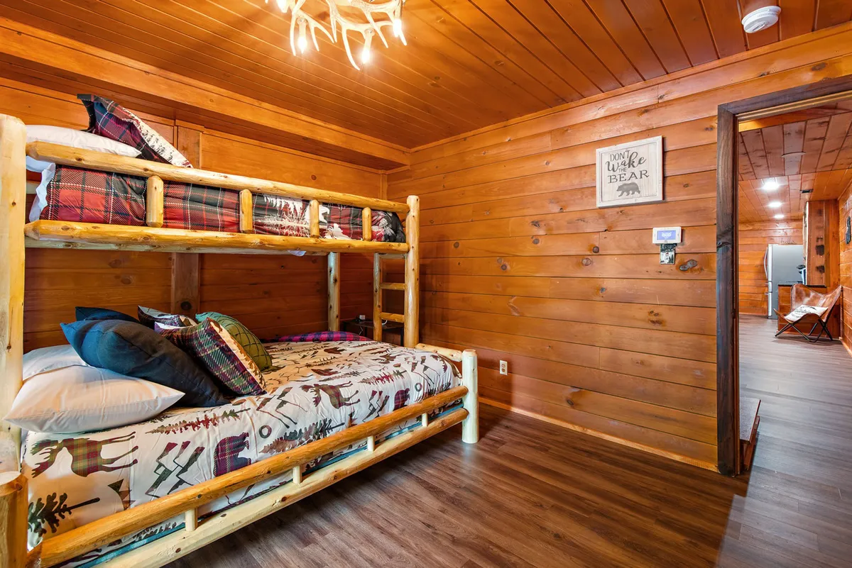A playful yet inviting bunk room with custom-built wooden bunk beds, decorative pillows, a whimsical antler chandelier, and soft lighting. The space feels perfect for sleepovers, storytelling, and family fun.