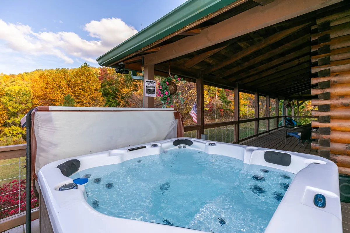 A cozy exterior shot focused on a hot tub surrounded by autumn foliage and the wooden structure of the cabin. The inviting water, lush trees, and natural ambiance create a sense of peace and immersion in nature.
