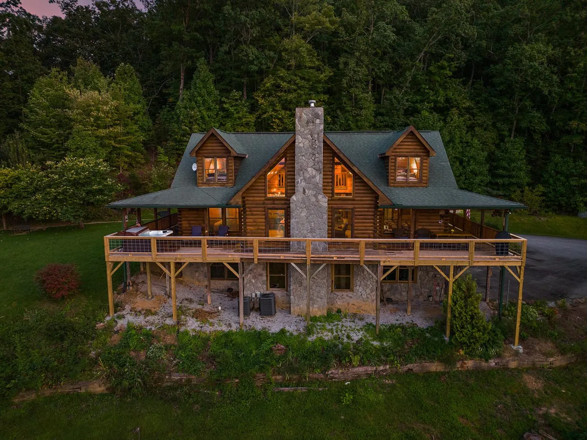 A tranquil exterior view of a log cabin with a spacious deck area and surrounding greenery. The deck is perfect for family meals, outdoor relaxation, and group activities, with ample room for everyone to be together.