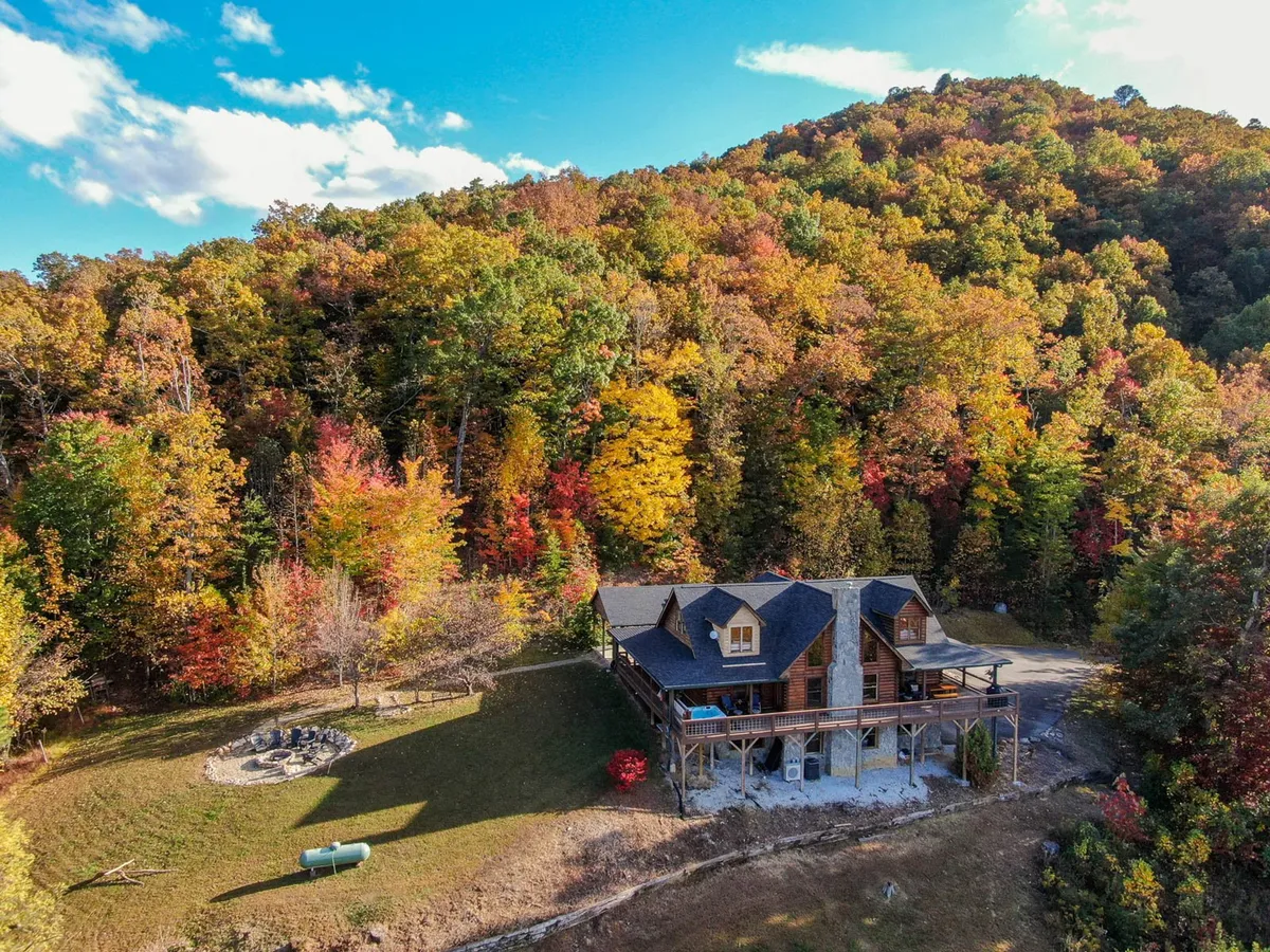 This photo features the log cabin surrounded by lush trees, with a welcoming fire pit area in the foreground. The setting is serene and invites guests to gather, share stories, and stargaze under the vast mountain sky. The cabin itself is nestled in nature, reinforcing the sense of a true mountain escape.